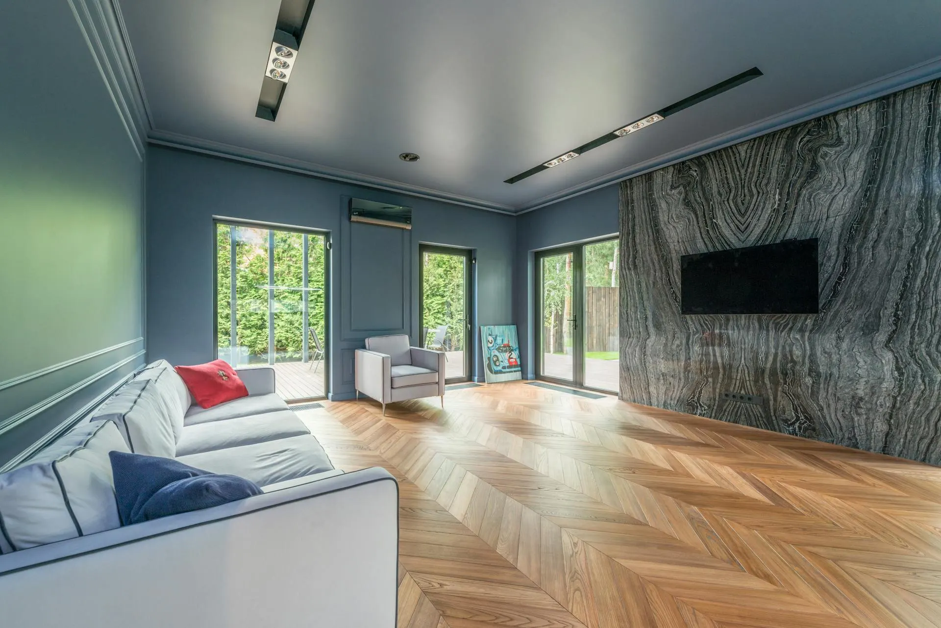 Modernes Wohnzimmer mit bodentiefen Fenstern und Terrassentüren, dahinter ein begrünter Garten