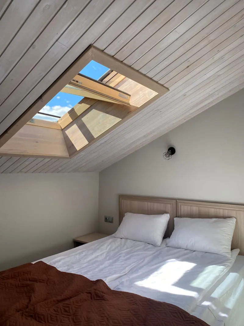 Geöffnetes Dachflächenfenster in der Dachschräge eines hellen Schlafzimmers unter dem Dach